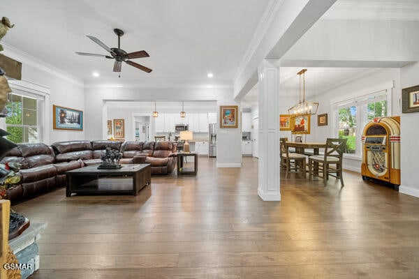 living room featuring crown molding, decorative columns, ceiling fan with notable chandelier, and hardwood / wood-style flooring