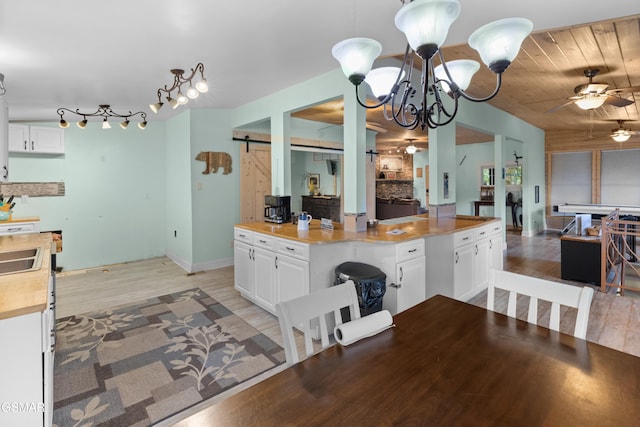 kitchen featuring light hardwood / wood-style floors, ceiling fan with notable chandelier, a barn door, and white cabinetry