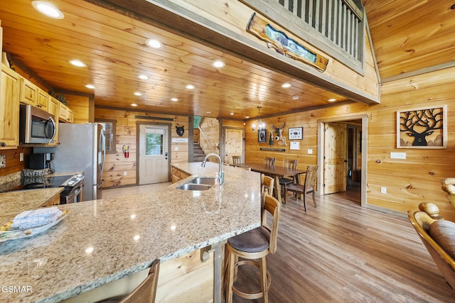 kitchen with a sink, stainless steel appliances, wood walls, light wood finished floors, and light stone countertops