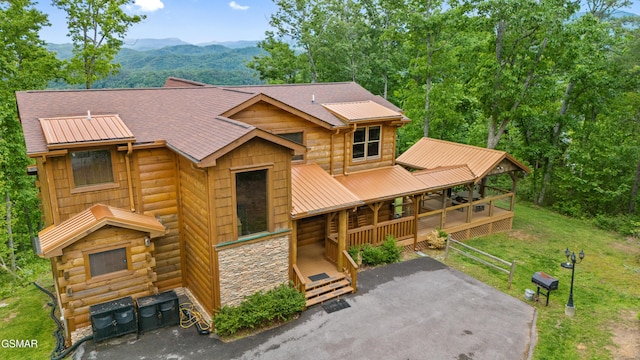 view of front of home with stone siding, a mountain view, metal roof, a front yard, and a porch