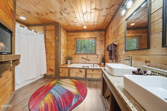 full bath featuring a garden tub, wooden walls, wood finished floors, and a sink