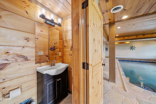 bathroom featuring vanity, visible vents, wooden ceiling, wooden walls, and stone finish flooring
