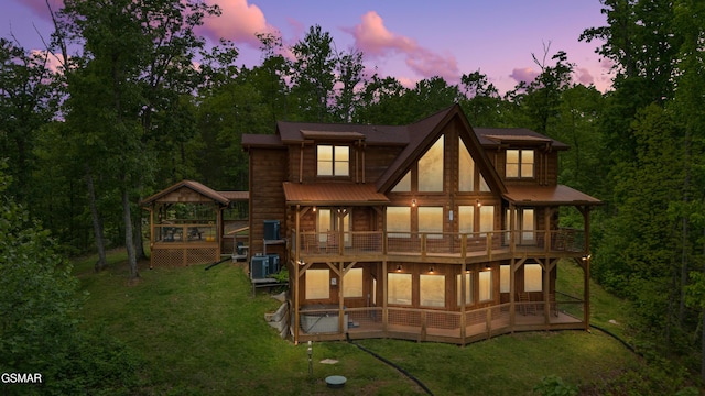 rear view of property featuring a sunroom, metal roof, central AC unit, a balcony, and a yard