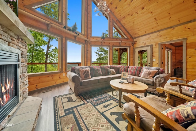 living area featuring a stone fireplace, wood walls, high vaulted ceiling, and plenty of natural light