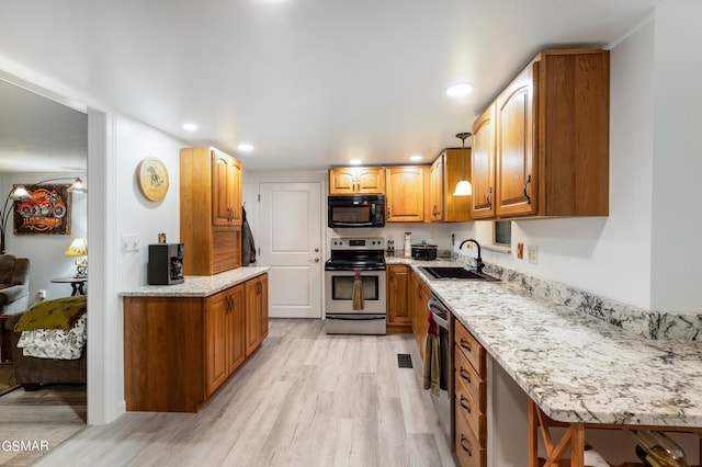 kitchen with appliances with stainless steel finishes, light stone counters, light hardwood / wood-style flooring, and sink