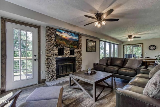 living area featuring a fireplace, dark wood-style flooring, ceiling fan, and a textured ceiling