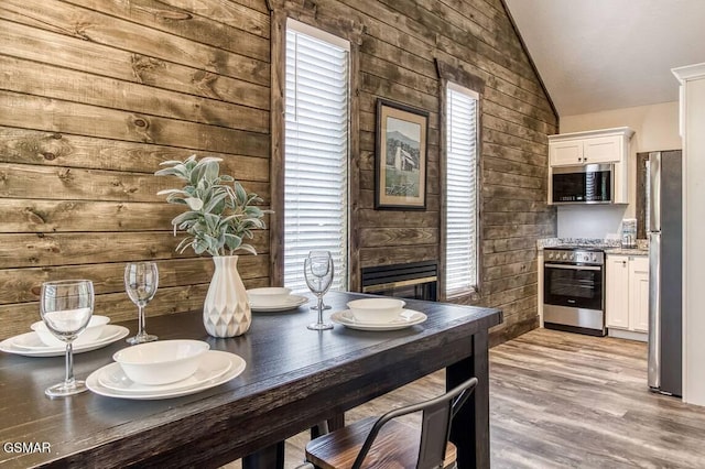 dining room with a wealth of natural light, light wood-type flooring, vaulted ceiling, and wooden walls