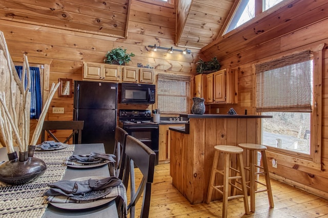 kitchen with wooden walls, black appliances, lofted ceiling, and light hardwood / wood-style floors