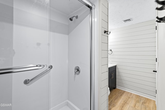 bathroom with a textured ceiling, wood finished floors, vanity, visible vents, and a stall shower