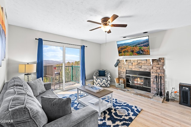 living area with ceiling fan, a textured ceiling, wood finished floors, and a stone fireplace