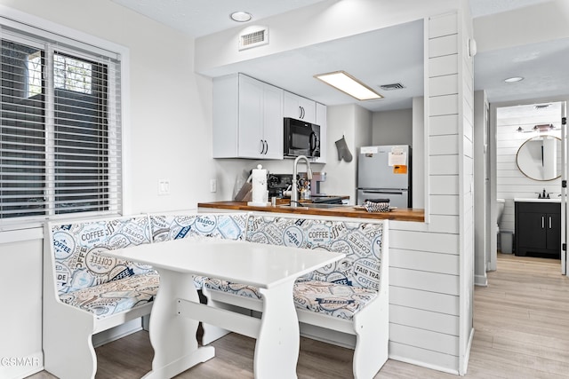 kitchen with black microwave, range with electric cooktop, visible vents, freestanding refrigerator, and breakfast area