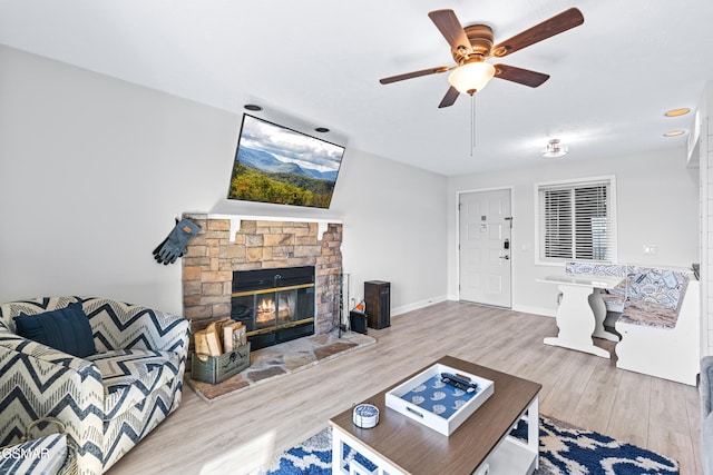 living room featuring ceiling fan, a fireplace, baseboards, and wood finished floors