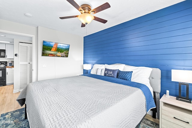 bedroom with light wood-style floors, wood walls, and a ceiling fan