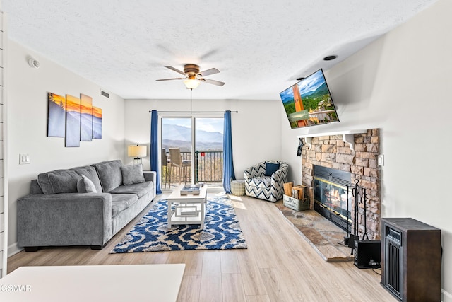 living room featuring a fireplace, visible vents, a ceiling fan, a textured ceiling, and wood finished floors