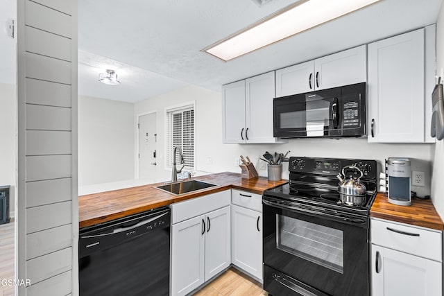 kitchen with black appliances, white cabinetry, wooden counters, and a sink