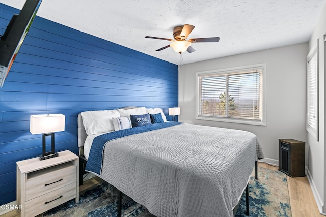 bedroom with a ceiling fan, a textured ceiling, baseboards, and wood finished floors