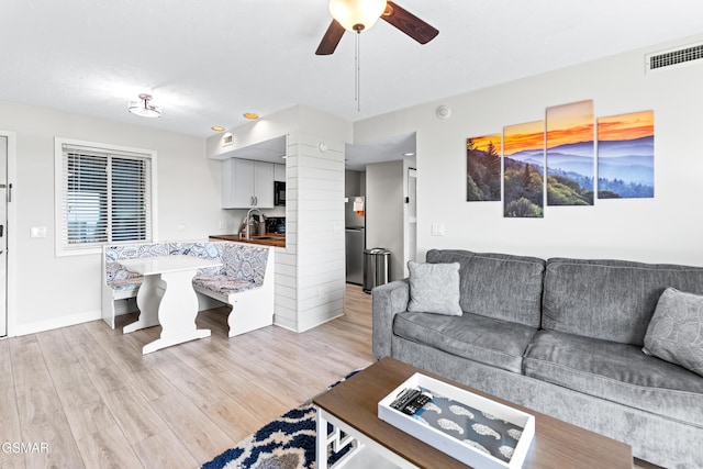 living area featuring ceiling fan, light wood-style flooring, visible vents, and baseboards