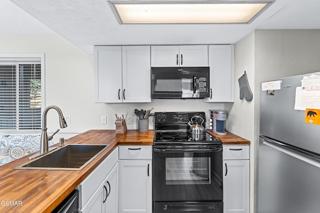 kitchen with black appliances, butcher block counters, white cabinetry, and a sink