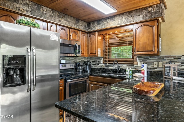 kitchen with decorative backsplash, brown cabinetry, appliances with stainless steel finishes, dark stone countertops, and a sink