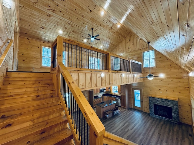 staircase with a stone fireplace, wood-type flooring, high vaulted ceiling, wooden ceiling, and wooden walls