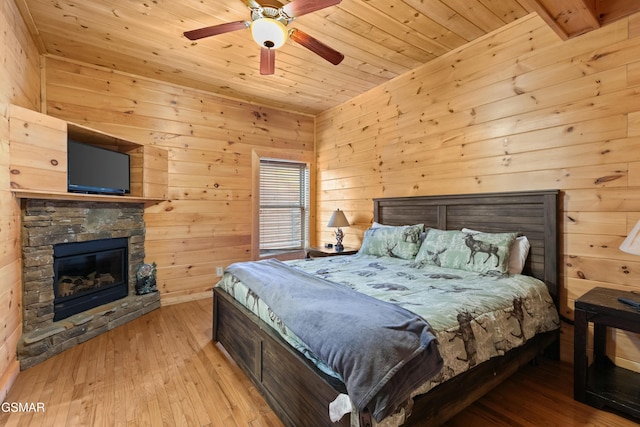 bedroom featuring wood ceiling, light hardwood / wood-style flooring, ceiling fan, a fireplace, and wood walls