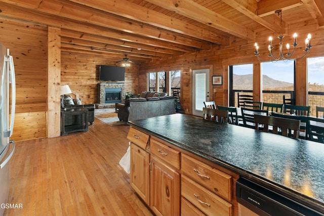 kitchen featuring wooden walls, a fireplace, light hardwood / wood-style floors, stainless steel dishwasher, and beamed ceiling