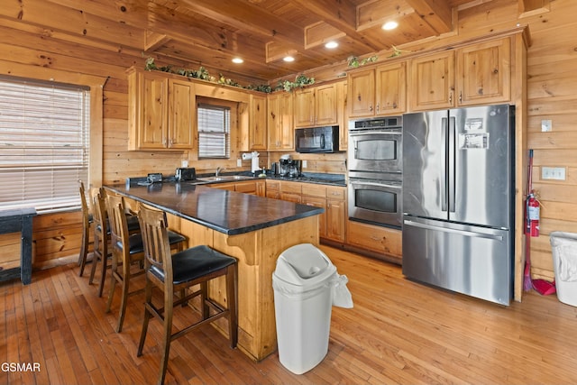 kitchen with stainless steel appliances, wooden walls, beam ceiling, and light hardwood / wood-style flooring