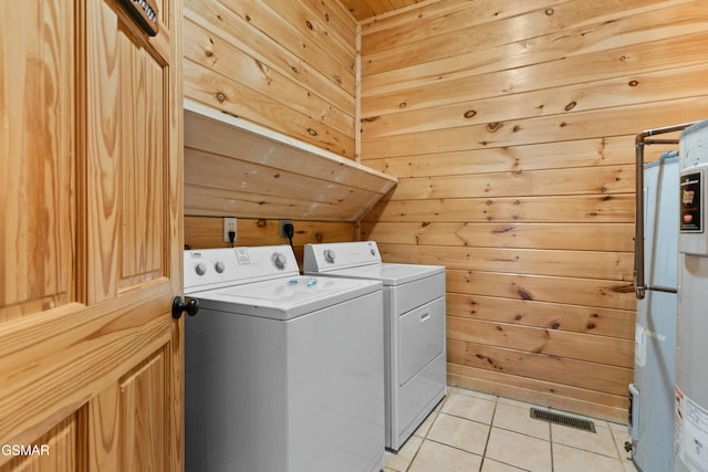 washroom with water heater, light tile patterned floors, washer and dryer, and wood walls