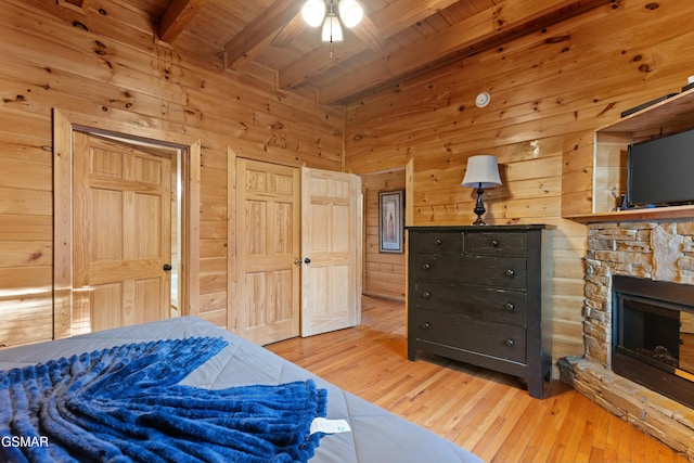 bedroom with beam ceiling, a fireplace, wooden walls, and light hardwood / wood-style flooring