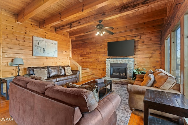 living room with wood ceiling, wooden walls, a stone fireplace, beamed ceiling, and light wood-type flooring