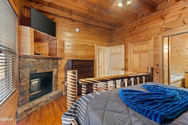 bedroom with hardwood / wood-style flooring, a stone fireplace, wooden ceiling, beamed ceiling, and wood walls