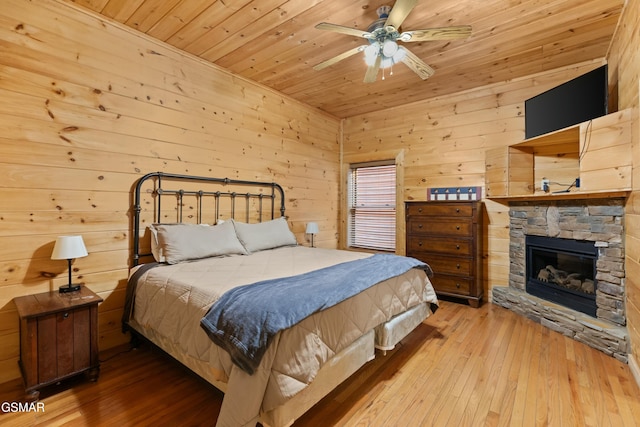 bedroom with wood ceiling, wooden walls, a stone fireplace, and light wood-type flooring