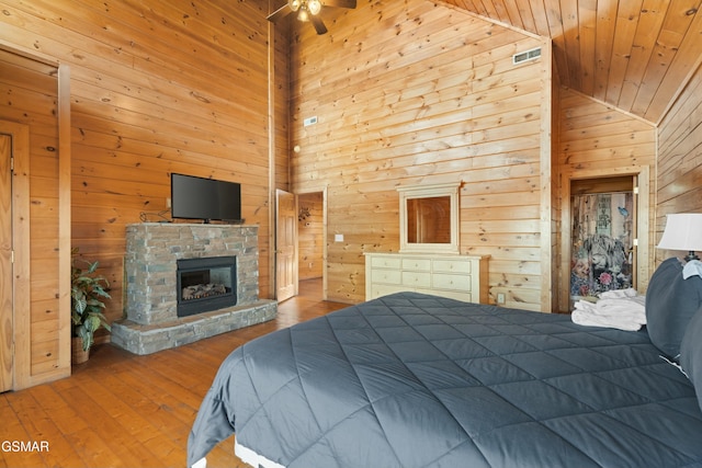 bedroom with a stone fireplace, high vaulted ceiling, wood walls, hardwood / wood-style flooring, and wooden ceiling