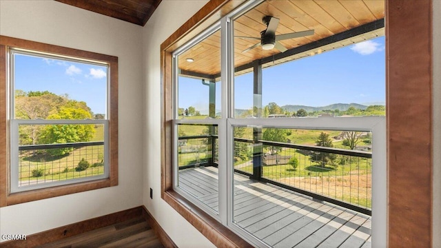 unfurnished sunroom with a mountain view, wooden ceiling, wood finished floors, and baseboards