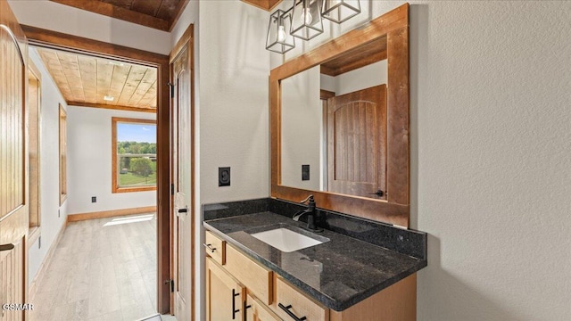 bathroom with a textured wall, baseboards, wooden ceiling, wood finished floors, and vanity