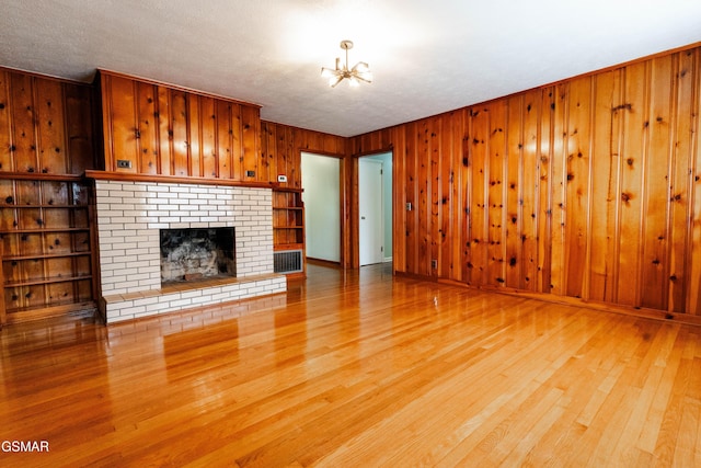 unfurnished living room featuring a textured ceiling, built in features, a notable chandelier, and a brick fireplace