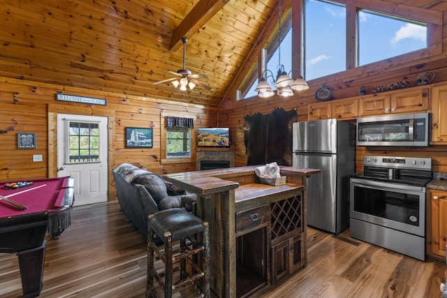 kitchen with beamed ceiling, high vaulted ceiling, stainless steel appliances, and wooden walls