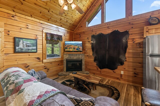 living room with lofted ceiling, wooden ceiling, a stone fireplace, wooden walls, and ceiling fan