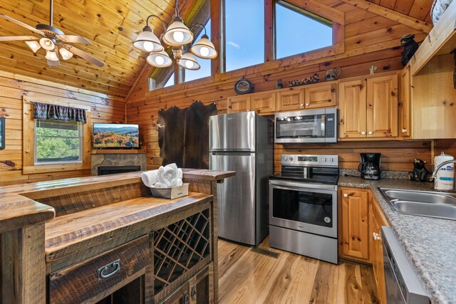 kitchen with high vaulted ceiling, light hardwood / wood-style floors, stainless steel appliances, and wooden walls