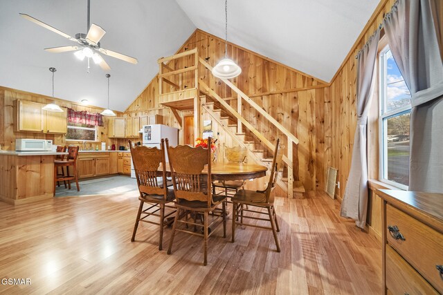 dining space featuring ceiling fan, sink, light hardwood / wood-style flooring, high vaulted ceiling, and wood walls