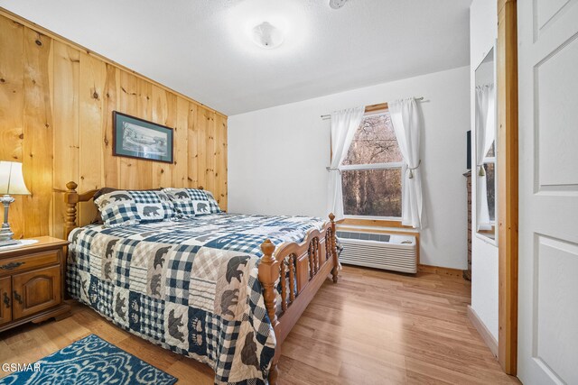 bedroom featuring light hardwood / wood-style floors, an AC wall unit, and wooden walls