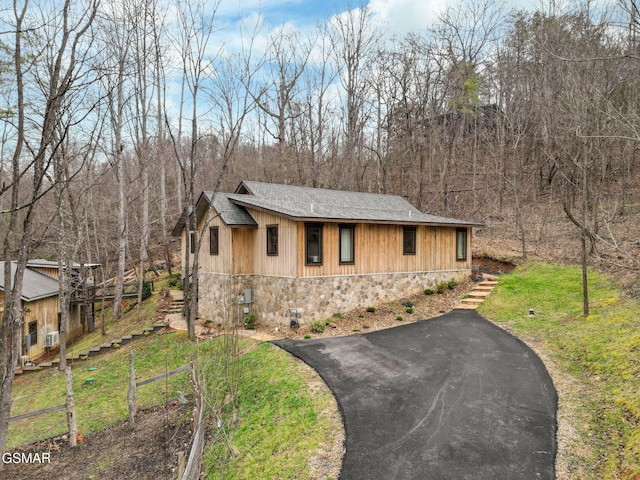 view of front of house with stairs, aphalt driveway, stone siding, and a front yard