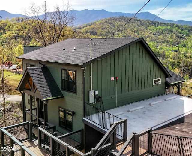 rear view of property with board and batten siding, roof with shingles, a deck with mountain view, and a forest view