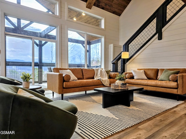 living area with wood-type flooring, wooden walls, a wealth of natural light, and high vaulted ceiling