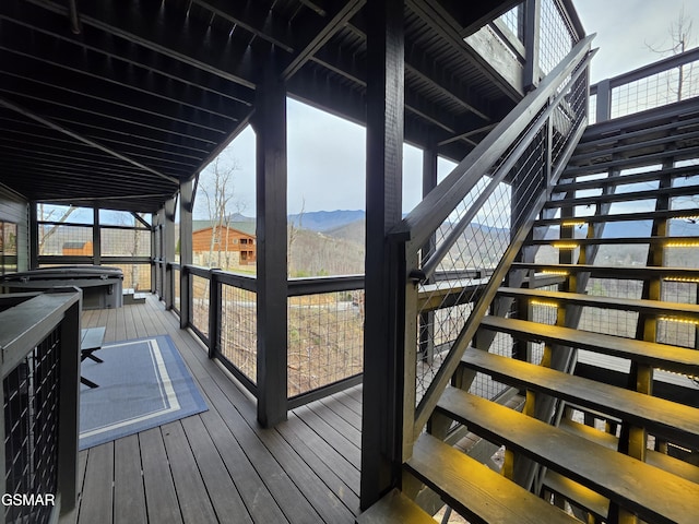 wooden terrace with a covered hot tub, a mountain view, and stairway