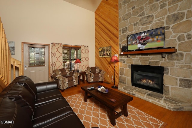 living room featuring a fireplace, wood-type flooring, high vaulted ceiling, and wood walls