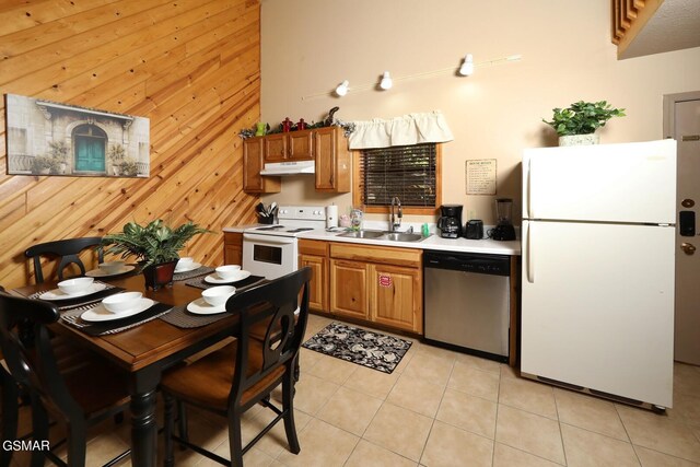 kitchen with light tile patterned flooring, white appliances, wooden walls, and sink