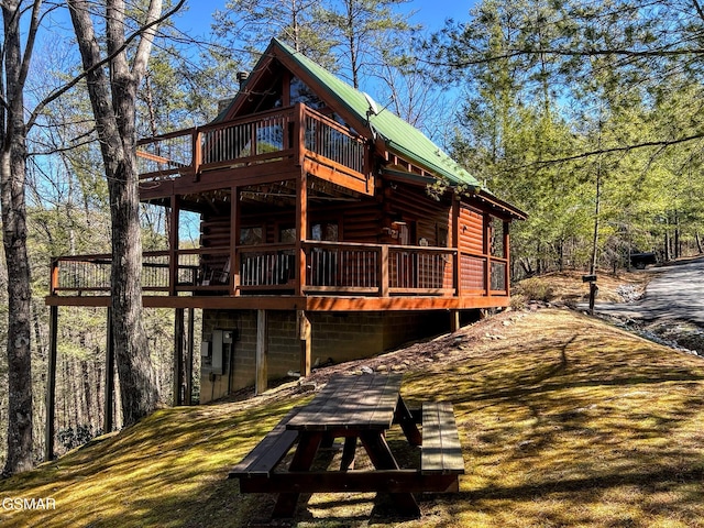 back of house featuring a deck, a lawn, a view of trees, and metal roof