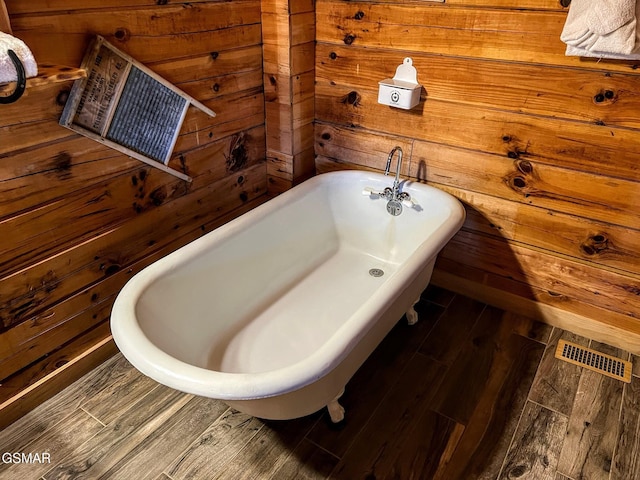 full bath with wooden walls, wood finished floors, visible vents, and a freestanding tub