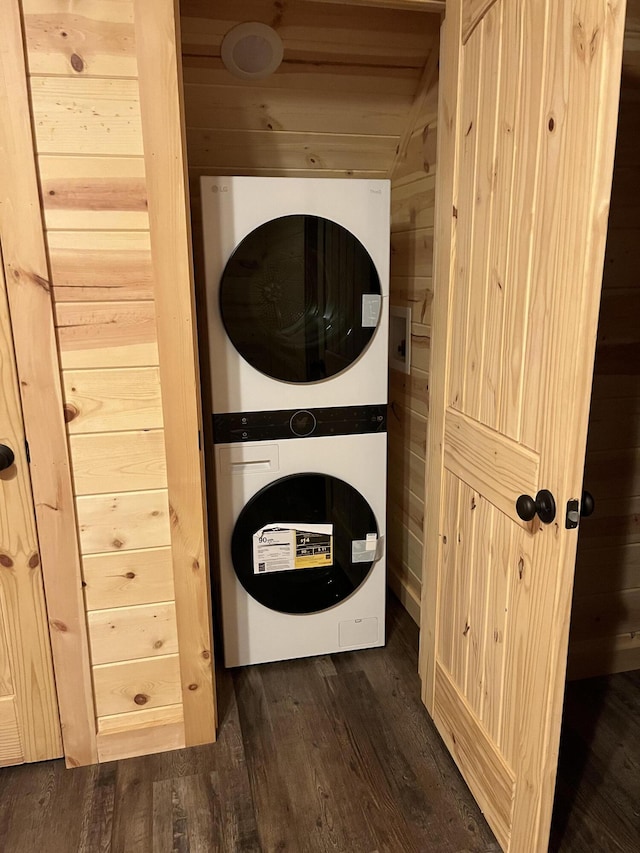 washroom with wood walls, dark hardwood / wood-style flooring, and stacked washer and clothes dryer